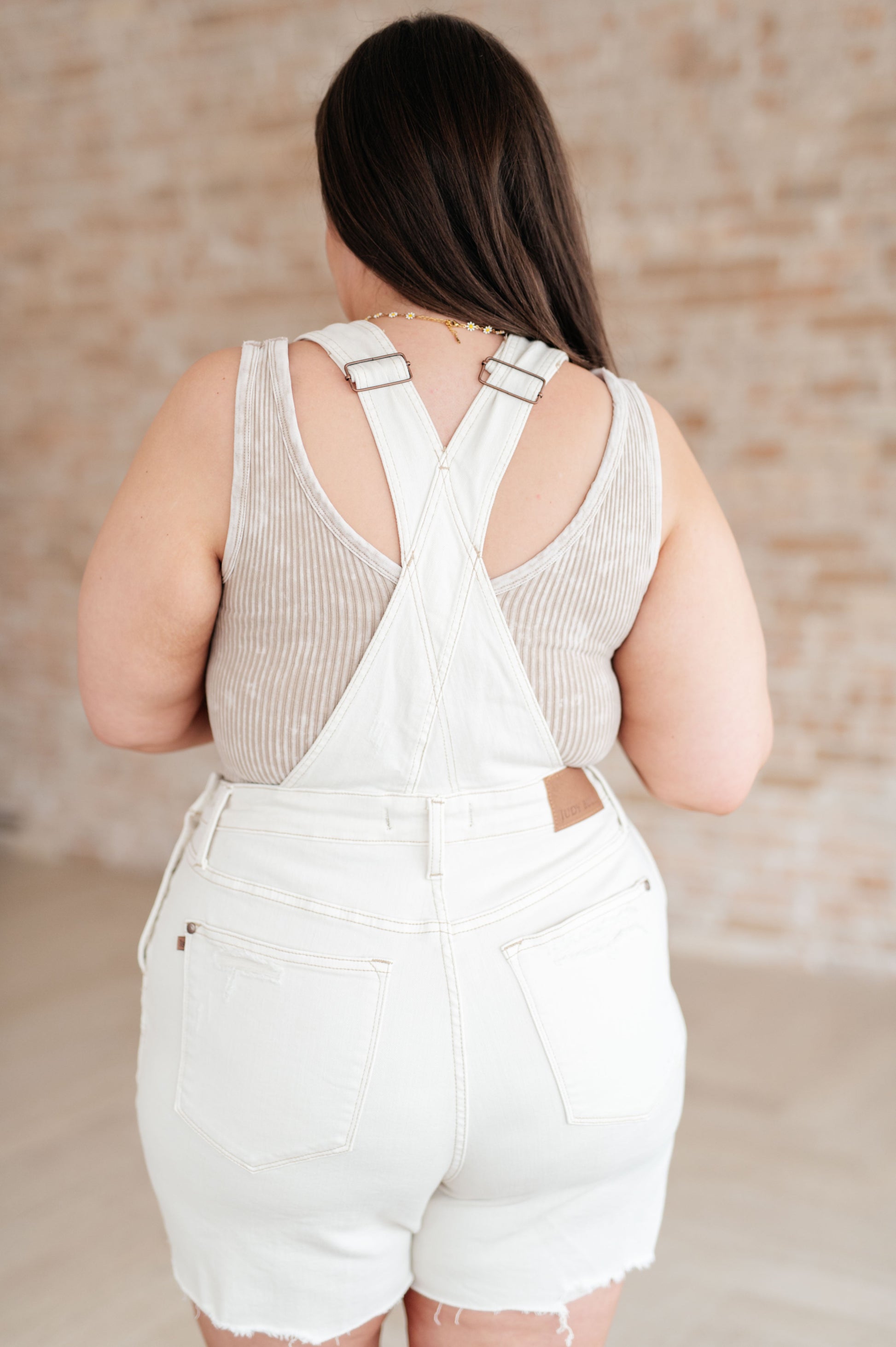back view of white jean short overalls with frayed edges 